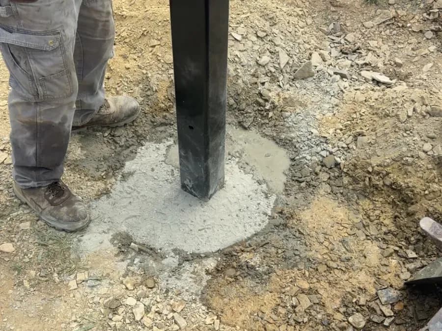 Steel gate post set plumb in fresh concrete on a black board-fence line