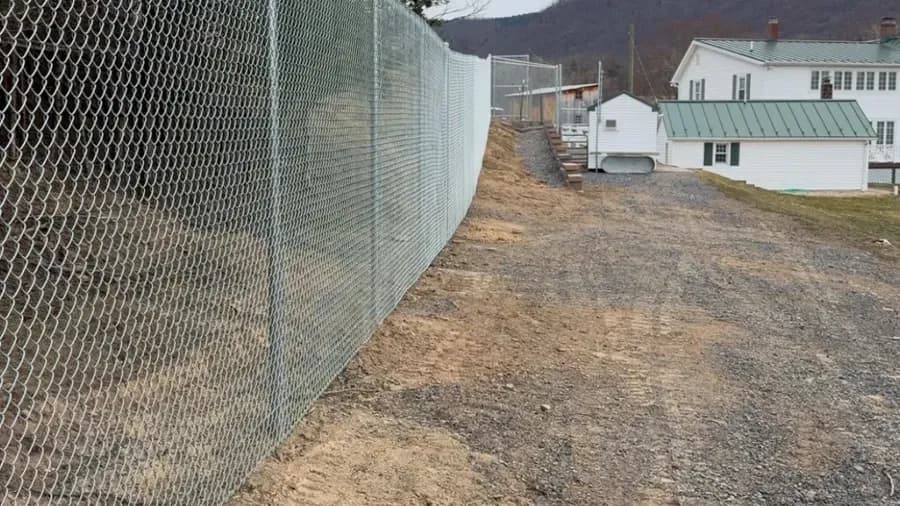 Tall galvanized chain-link security fence line along a gravel drive