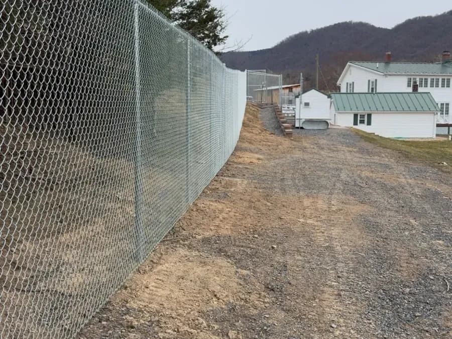 Tall galvanized chain-link security fence line along a gravel drive