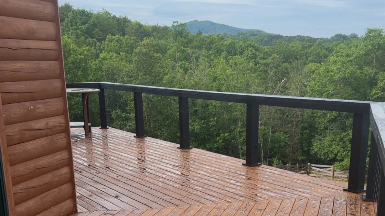 Custom-stained wood deck with black cable railing overlooking wooded mountains