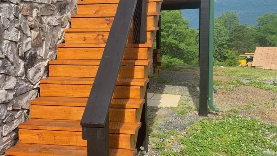 Freshly stained wood stairs with black handrail beside a stone foundation