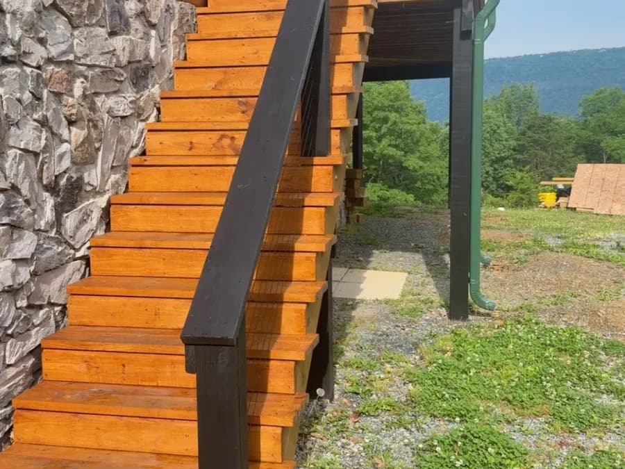 Freshly stained wood stairs with black handrail beside a stone foundation