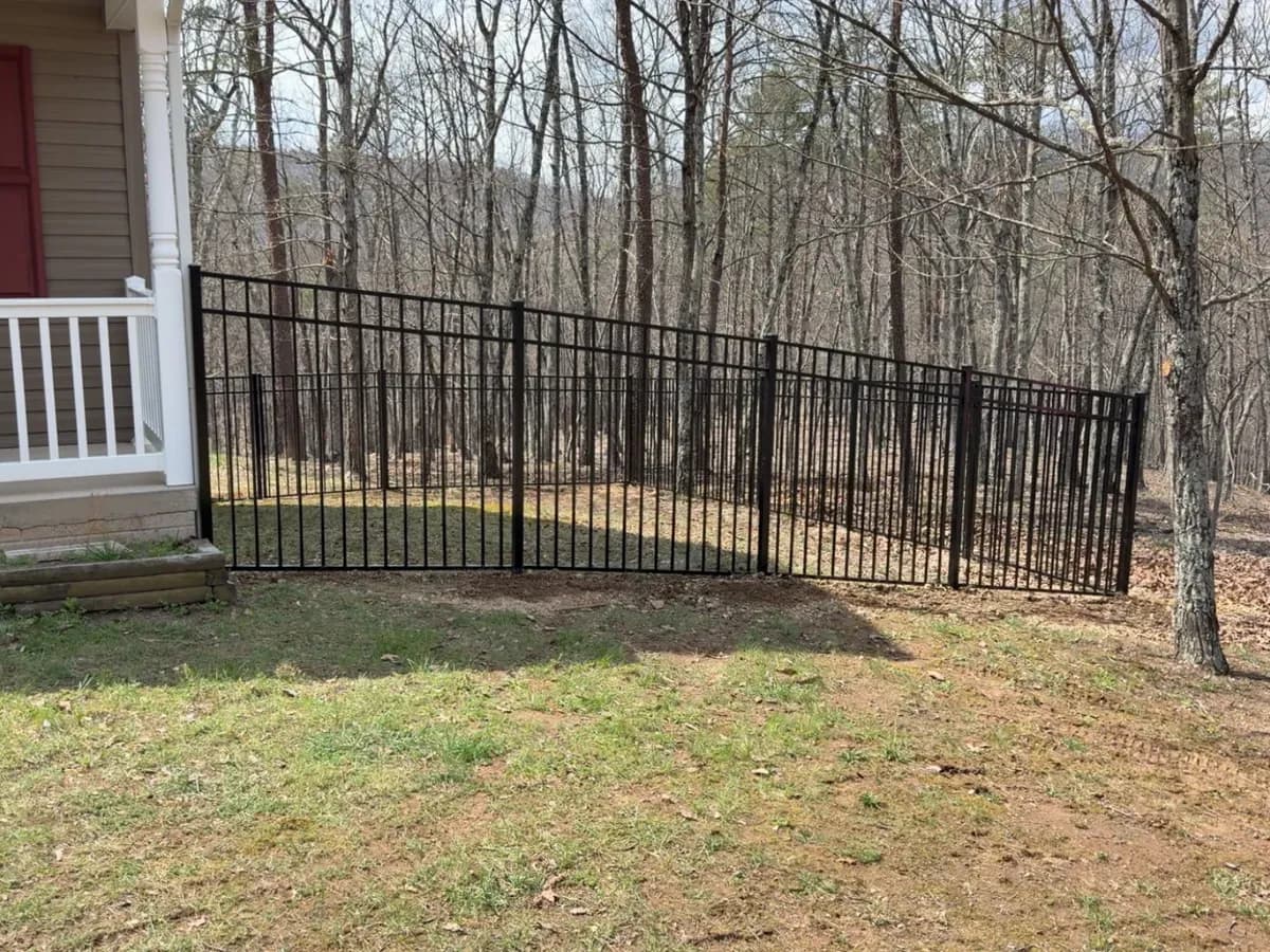 Black ornamental metal fence line along a wooded backyard
