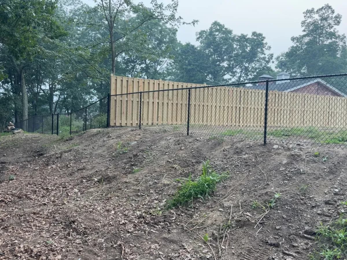 New vertical-board wood fence with black chain-link yard fencing